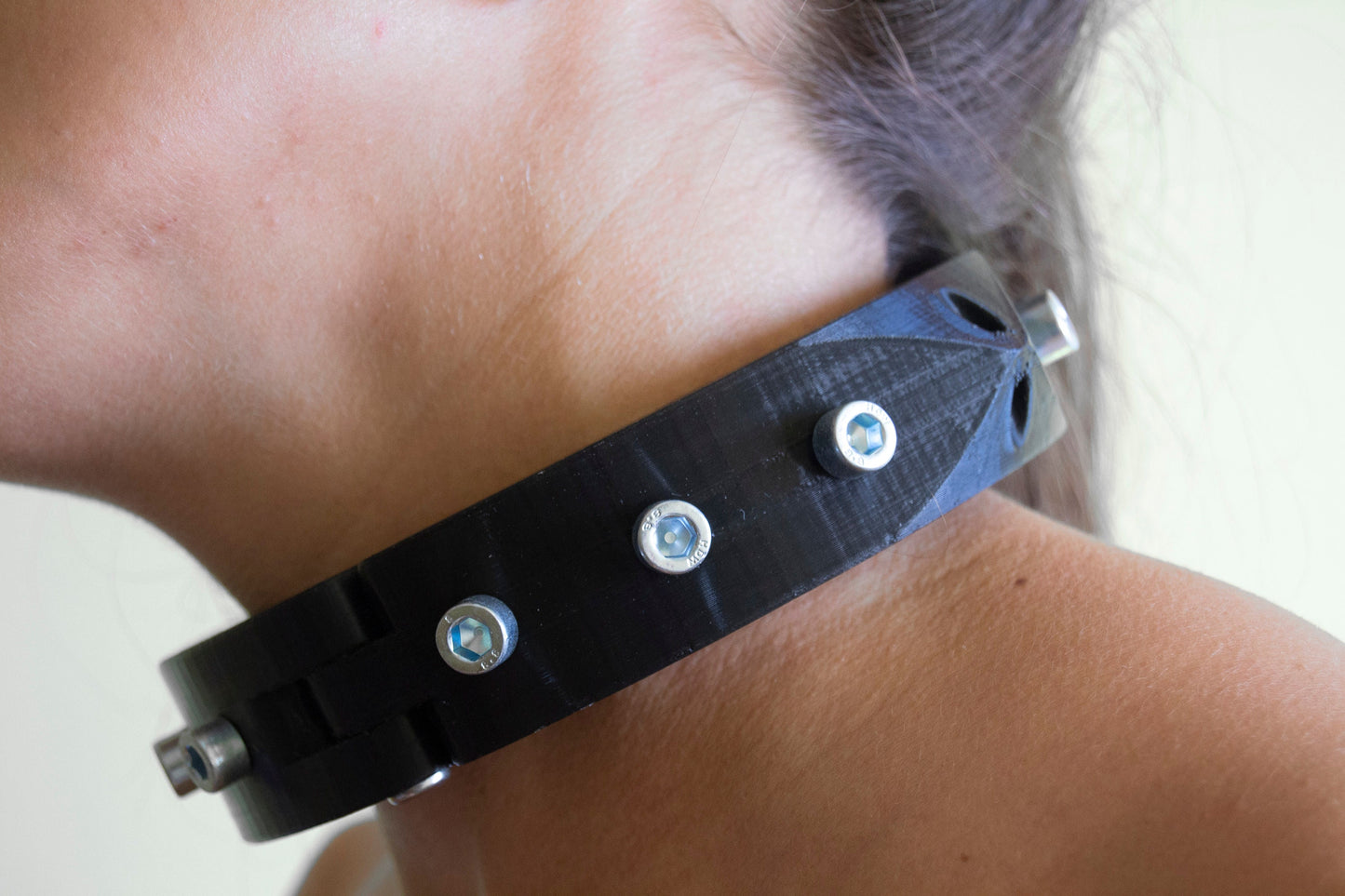 Girl wearing black  3d printed bdsm collar adorned with bolts seen from the side